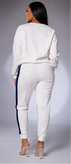 A woman modeling a matching white sweatshirt and jogger set in three views: front, back, and side. The outfit features a wide navy blue stripe across the chest, red accents on the upper sleeve and upper thigh, and navy blue side stripes on the joggers.