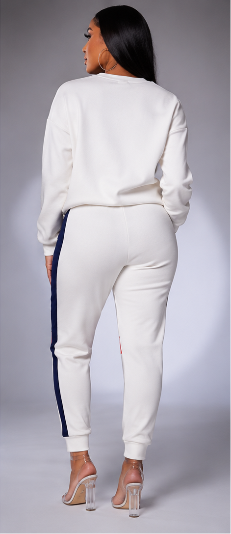 A woman modeling a matching white sweatshirt and jogger set in three views: front, back, and side. The outfit features a wide navy blue stripe across the chest, red accents on the upper sleeve and upper thigh, and navy blue side stripes on the joggers.