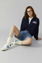 Woman wearing a navy sports jacket and denim shorts on a beige background