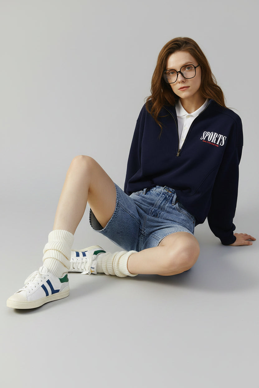 Woman wearing a navy sports jacket and denim shorts on a beige background