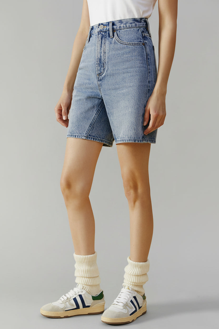 Person wearing light blue denim shorts and white sneakers on a beige background