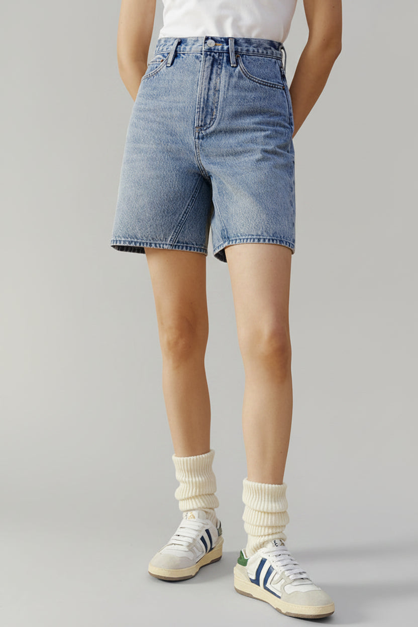 Person wearing blue denim shorts and white sneakers on a beige background