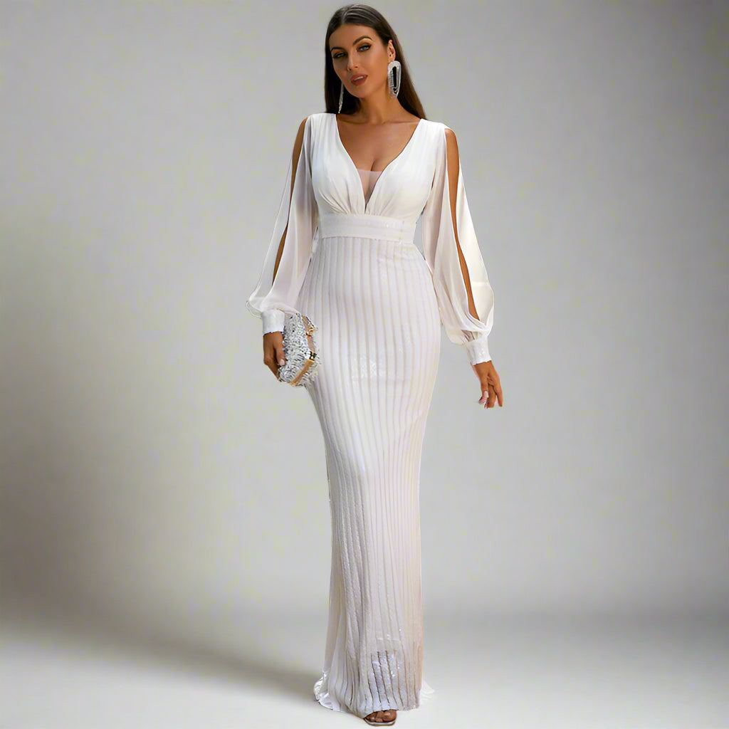 Woman in a white dress standing on a balcony with a table and chairs in the background.