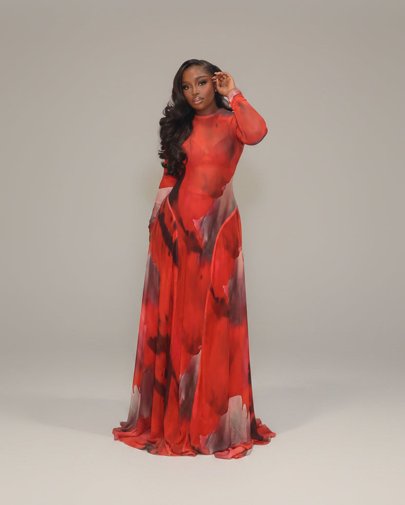Woman in a red and black patterned dress standing against a white curtain.