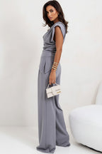 Woman wearing a gray jumpsuit holding a white handbag on a plain background