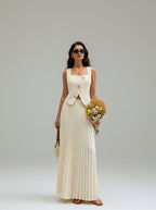 Woman in a long white dress holding flowers and a yellow bag on a city street.
