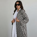 Woman wearing a black and white houndstooth patterned coat against a plain background