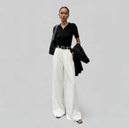 Woman wearing a black top and white pants against a gray background