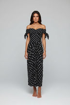 Woman in a black polka dot dress standing against a stone wall.