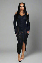 Woman wearing a black dress with a slit, standing against a neutral background.