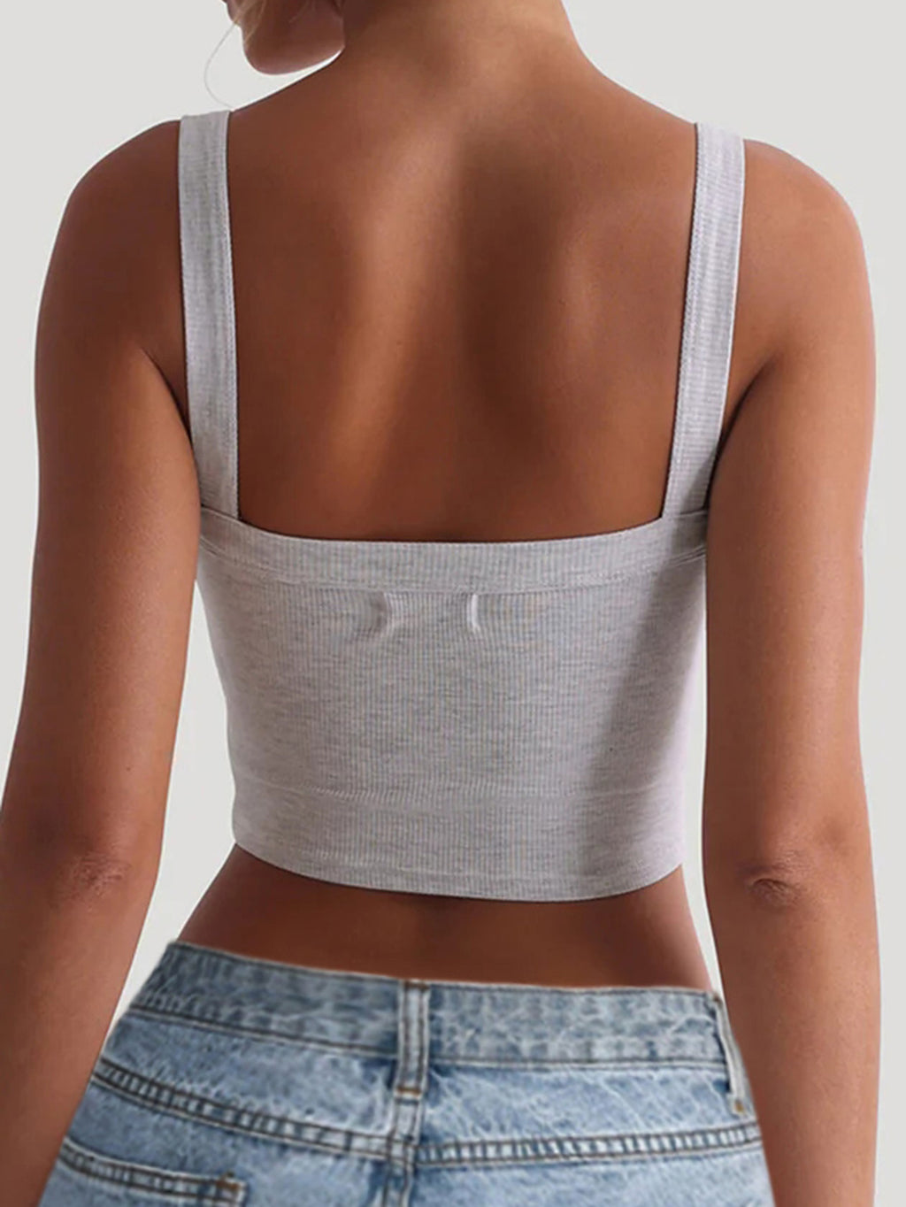 Person wearing a gray tank top and blue jeans on a plain background