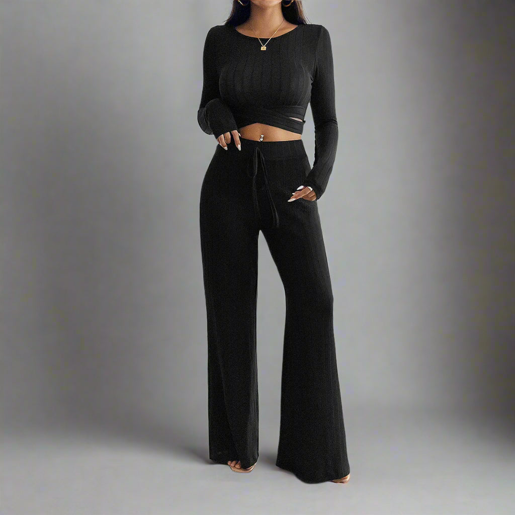 Person wearing a black long-sleeve top and wide-leg pants in a minimalistic room.