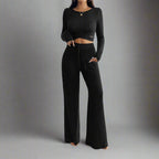Person wearing a black long-sleeve top and wide-leg pants in a minimalistic room.