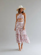 Woman in a floral dress and hat standing in a bright room with large windows.