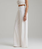 Person wearing a white outfit with wide-leg pants on a plain background