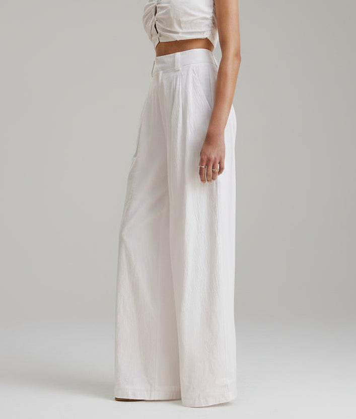 Person wearing a white outfit with wide-leg pants on a plain background