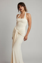 Woman in a beige evening gown standing on a balcony with greenery and water in the background