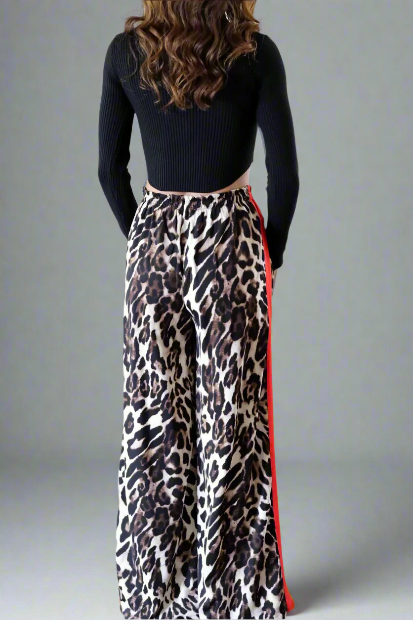 Person wearing a black top and leopard print skirt with red trim in a room.