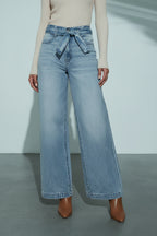 Person wearing light blue wide-leg jeans with a belt against a neutral background