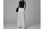 Person wearing a navy top and white wide-leg pants, standing in a doorway.