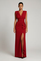 Woman wearing a red evening gown with a high slit against a white wall.
