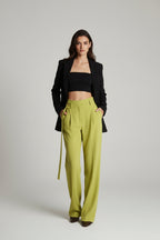 Woman wearing a black blazer and bright green pants in an elegant room.