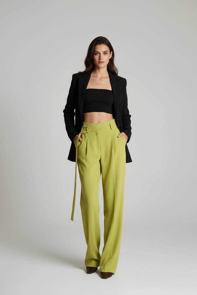 Woman wearing a black blazer and bright green pants in an elegant room.