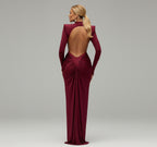 Woman in a burgundy evening gown standing against a stone wall.