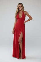 Woman wearing a red halter neck gown with a high slit on a plain background