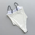 White swimsuit with black straps on a gray surface with decorative elements.