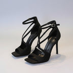 Black high-heeled sandals with strappy design on a white surface.