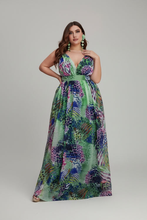 Woman in a colorful floral dress standing next to pink flowers indoors.