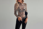 Person wearing a leopard print long-sleeve top and black pants in a room with white furniture and decor.