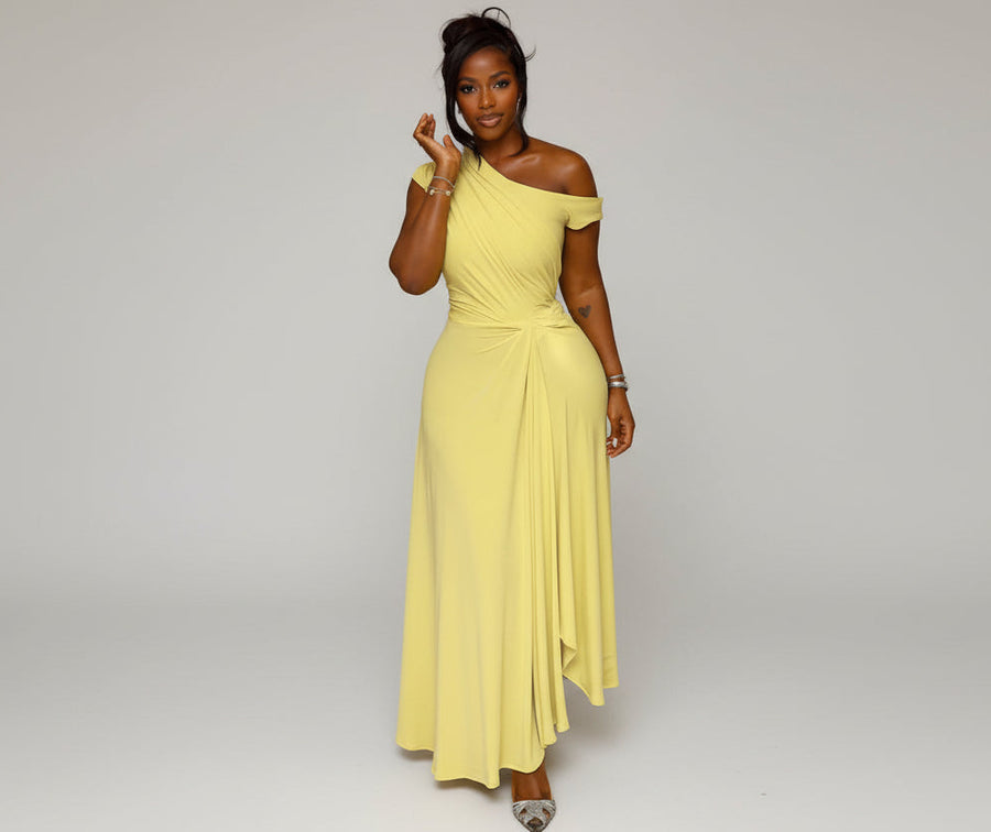 Woman in a yellow one-shoulder dress standing in front of beige curtains.