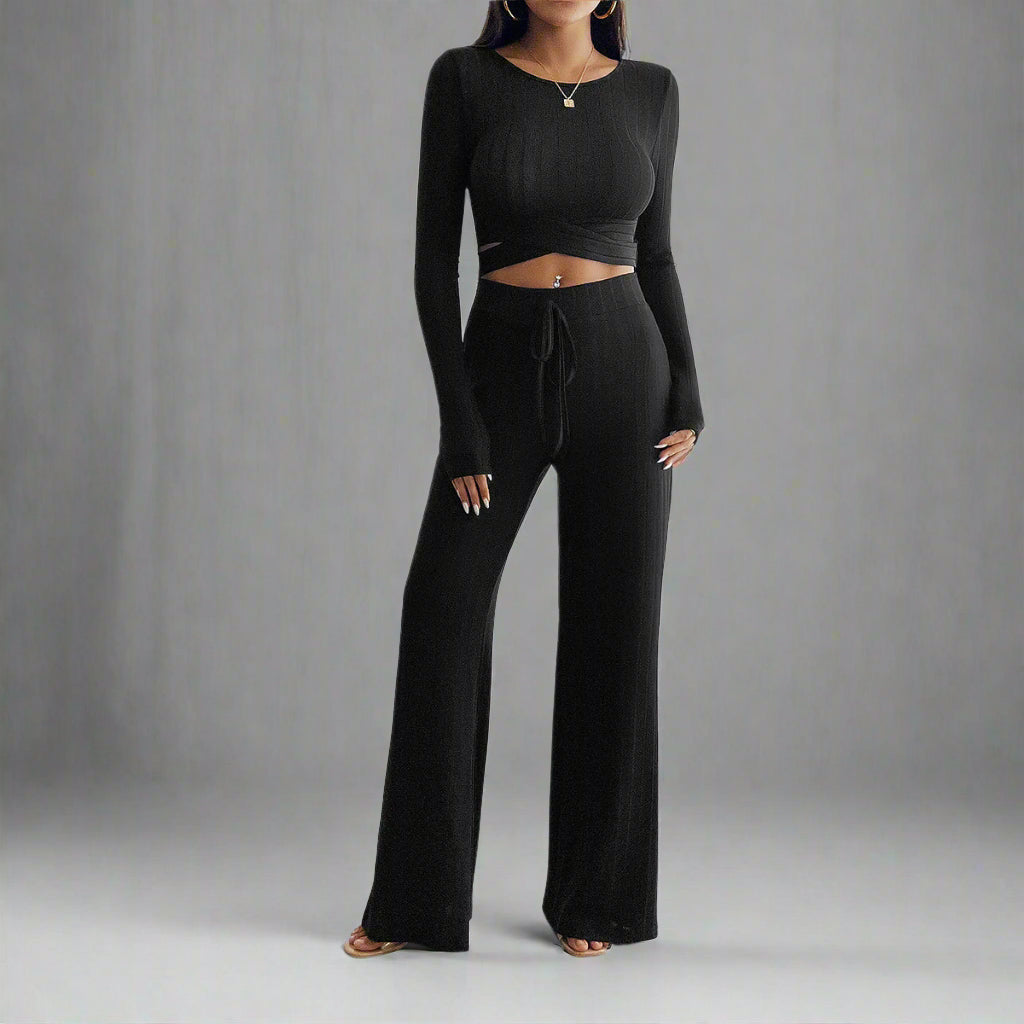 Person wearing a black long-sleeve top and wide-leg pants in a minimalistic room.