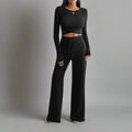 Person wearing a black long-sleeve top and wide-leg pants in a minimalistic room.