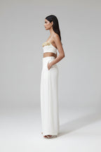 Woman in a white outfit with gold embellishments standing in a modern indoor setting.