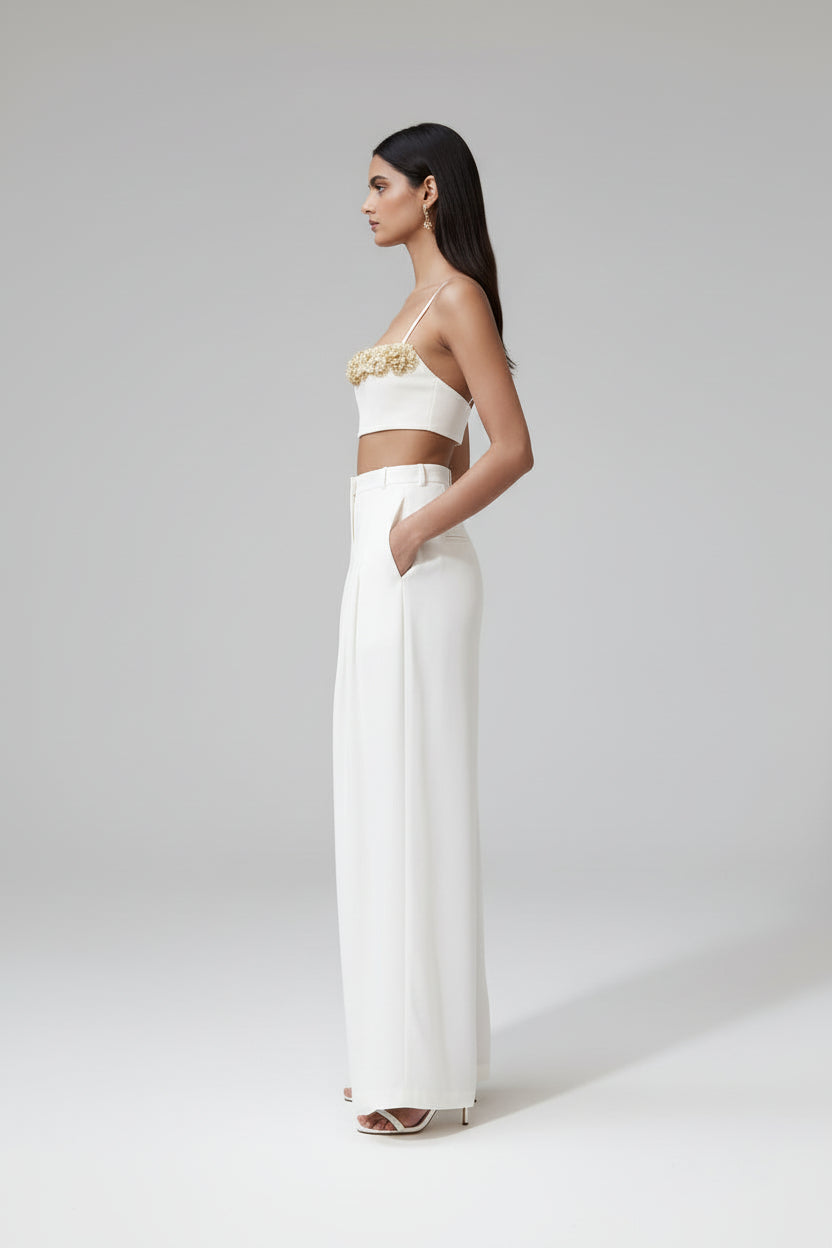 Woman in a white outfit with gold embellishments standing in a modern indoor setting.