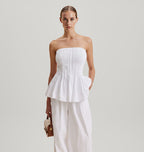Woman wearing a white strapless top and white pants against a plain background