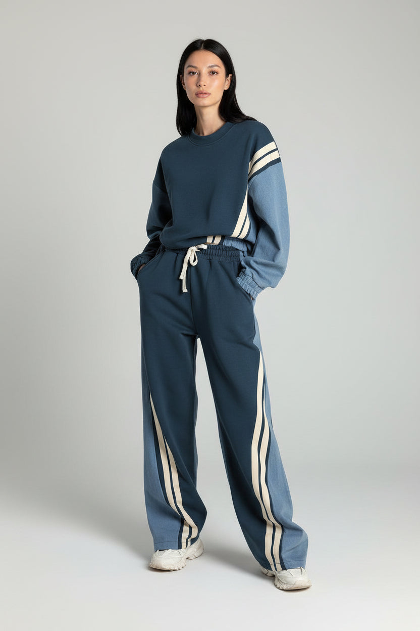 Person wearing a blue tracksuit with white stripes against a concrete wall.