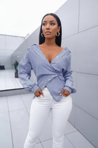 Woman wearing a blue and white striped wrap blouse with white pants indoors.