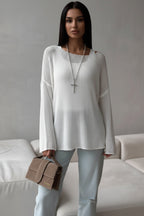 Person wearing a white sweater and light blue pants holding a brown handbag against a neutral background.