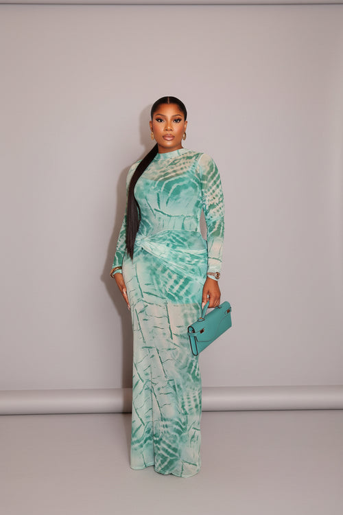 Woman in a patterned dress holding a clutch against a wooden wall.