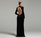 Woman in a black evening gown with a high slit standing against a dark wall.