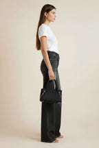 Person wearing black high-waisted jeans and holding a black handbag in an indoor setting.