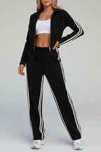 Person wearing a black tracksuit with white stripes standing in front of a wooden bench.
