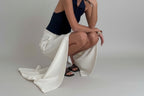 Person wearing a navy top and white skirt sitting on the floor.