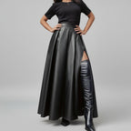 Person wearing a black leather skirt and boots against a gray building background