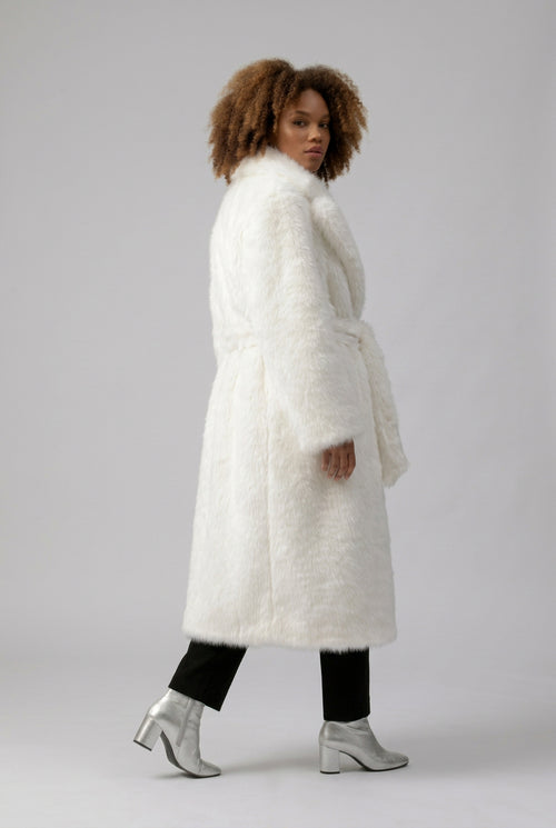 A model wearing a white faux fur coat with a casual fit, featuring a belted waist and a hook closure. The model has sunglasses and is standing against a grey background.