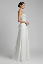 Woman wearing a strapless, embellished wedding gown with a plain background